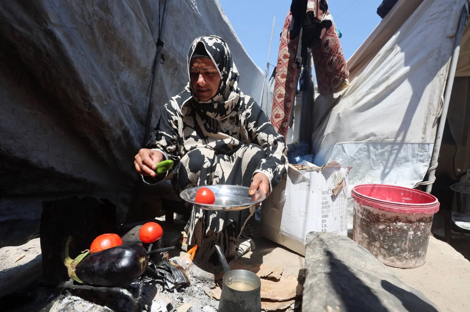 Displaced Palestinian woman Nisreen Abu Saada cook vegetables over a wood fire outside her tent, amid shortages of lighters and cooking gas, in Khan Younis, in the southern Gaza Strip, July 21, 2026. REUTERS/Ramadan Abed
