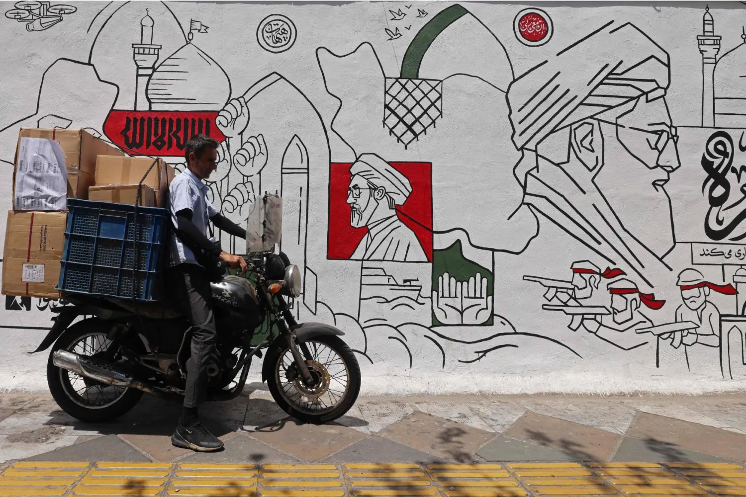 TOPSHOT - A motorist parks his bike in front of a wall mural along the street in Tehran on July 21, 2026. (Photo by ATTA KENARE / AFP) / 
