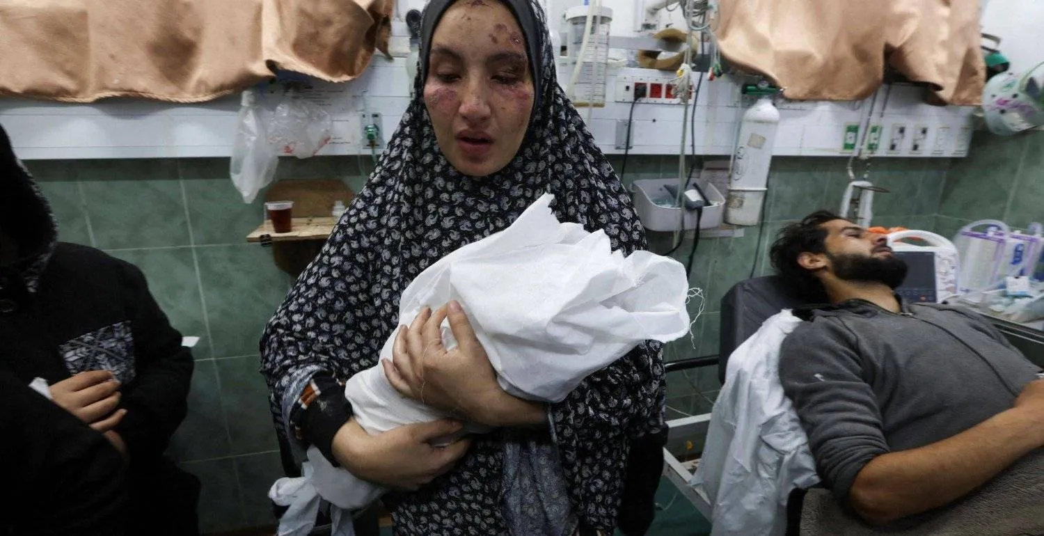 سيدة فلسطينية مصابة تحمل طفلها حديث الولادة بأحد مستشفيات غزة (رويترز)
