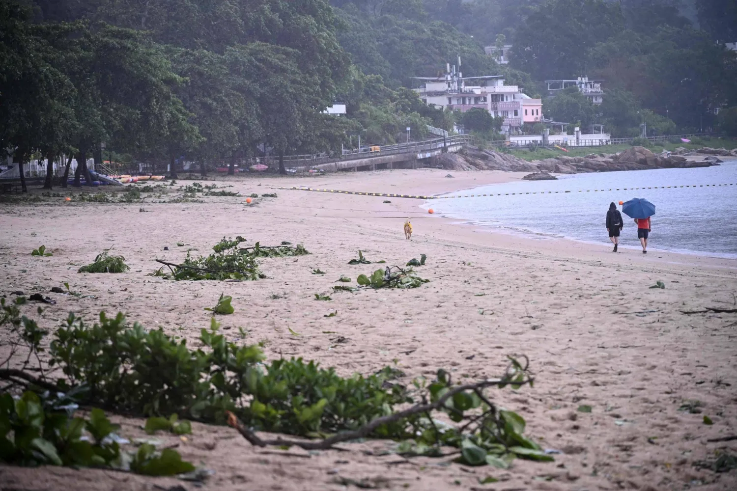 People walk on a beach with debris from Typhoon Noul which passed close to Hong Kong on July 26, 2026. (Photo by Peter PARKS / AFP)