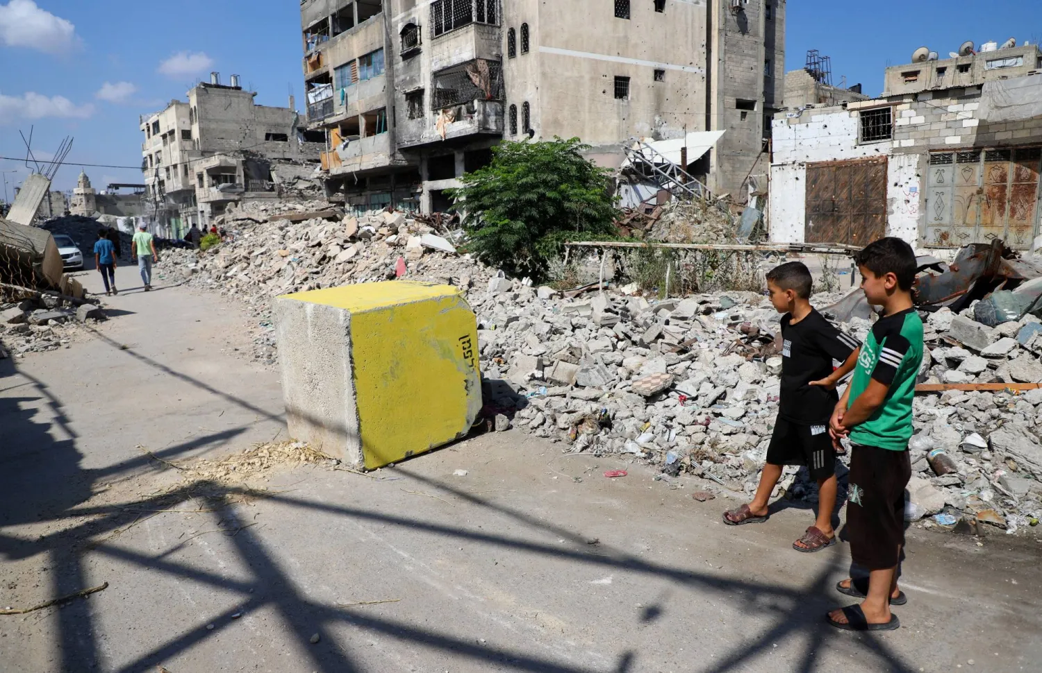 فتيان فلسطينيون ينظرون إلى كتلة خرسانية صفراء تُشير إلى «المنطقة الصفراء» الخاضعة للسيطرة العسكرية الإسرائيلية في حي طفاح بمدينة غزة (رويترز)