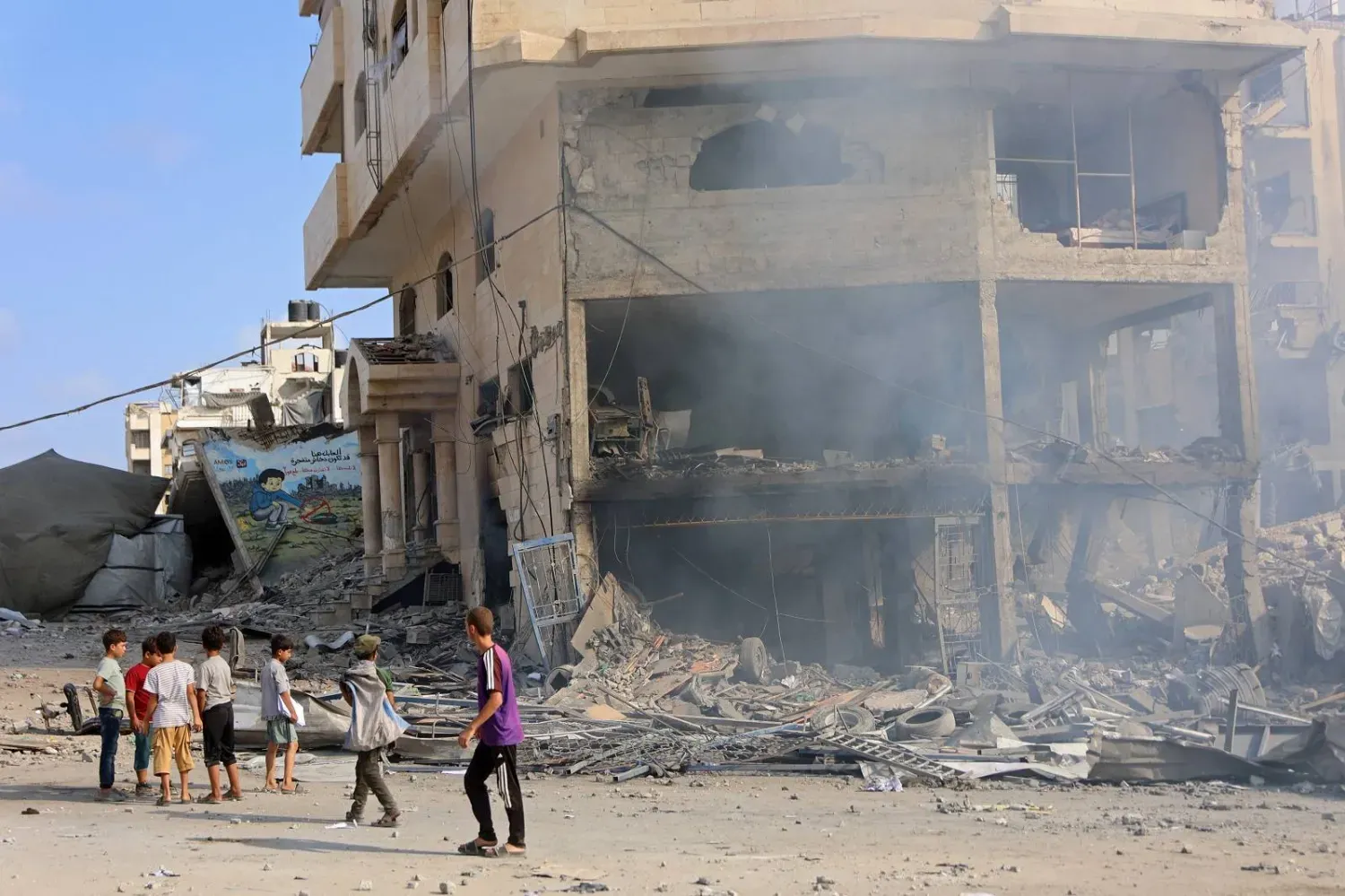 İsrail'in Gazze şehrine düzenlediği hava saldırısının ardından El-Calaa Caddesi'nde yıkılmış bir binanın yanında duran Filistinli çocuklar (AFP)