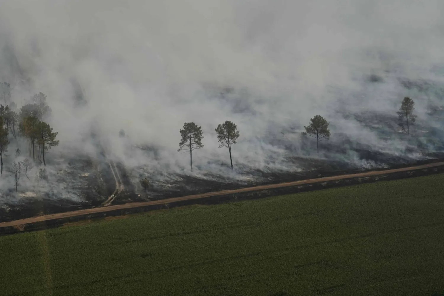 This aerial view taken from a Civil Security helicopter shows smoke billowing from a burning forested area next to a field near Ares, southwestern France, on July 28, 2026. (AFP)