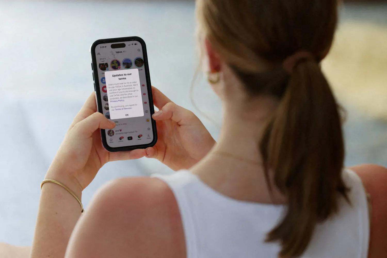 A teenager poses holding a mobile phone displaying a message from TikTok as law banning social media for users under 16 in Australia takes effect, in Sydney, Australia, December 10, 2025. (Reuters)
