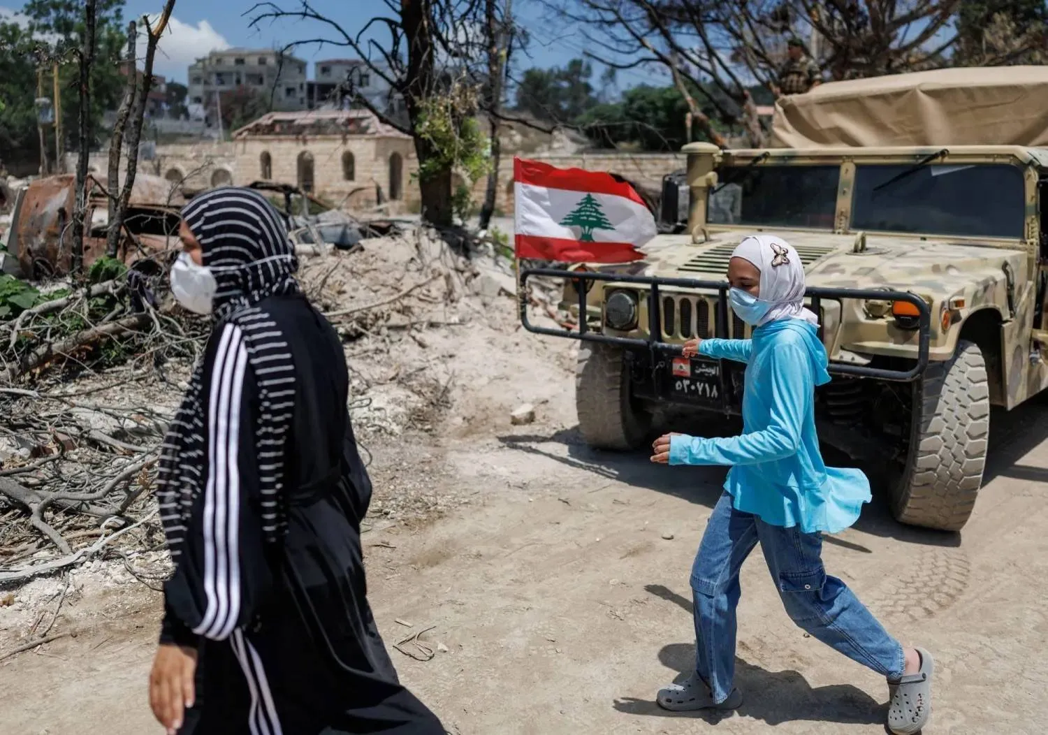 Two women walk past a Lebanese Army armored vehicle during the army’s deployment in the first pilot area in Zawtar al-Gharbiyeh. (Reuters) 