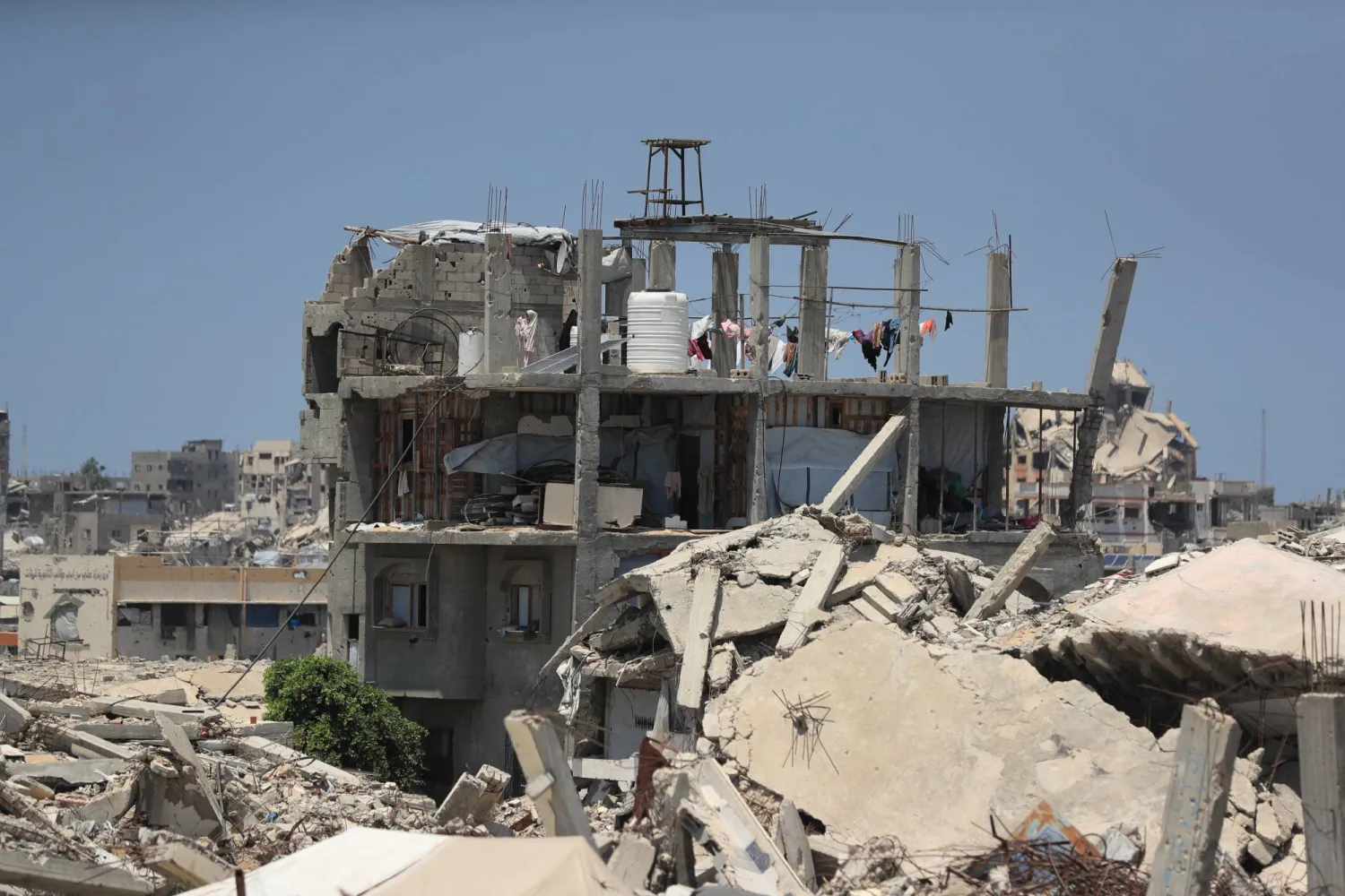 A Palestinian woman stands on the roof of a house damaged during the war, surrounded by destroyed buildings, in Gaza City, August 1, 2026. (Reuters)