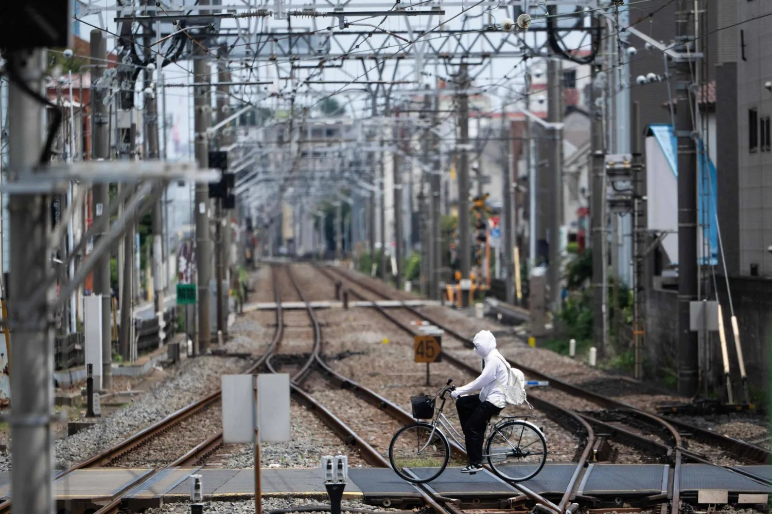 A woman covers up to protect from the sun as she bikes across a railroad track on a hot day in Tokyo on July 31, 2026. (Photo by Andrew CABALLERO-REYNOLDS / AFP)