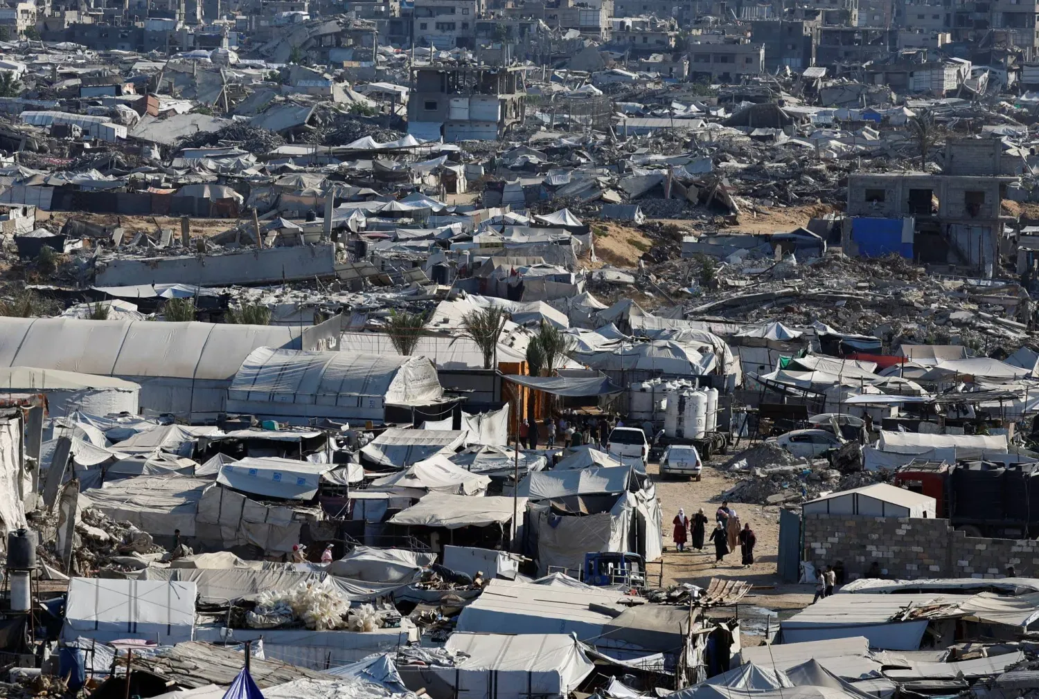 Filistinliler, Gazze Şeridi'nin kuzeyindeki Cibaliye mülteci kampında savaş sırasında yıkılan konut binalarının enkazı arasında yürüyor (Reuters)