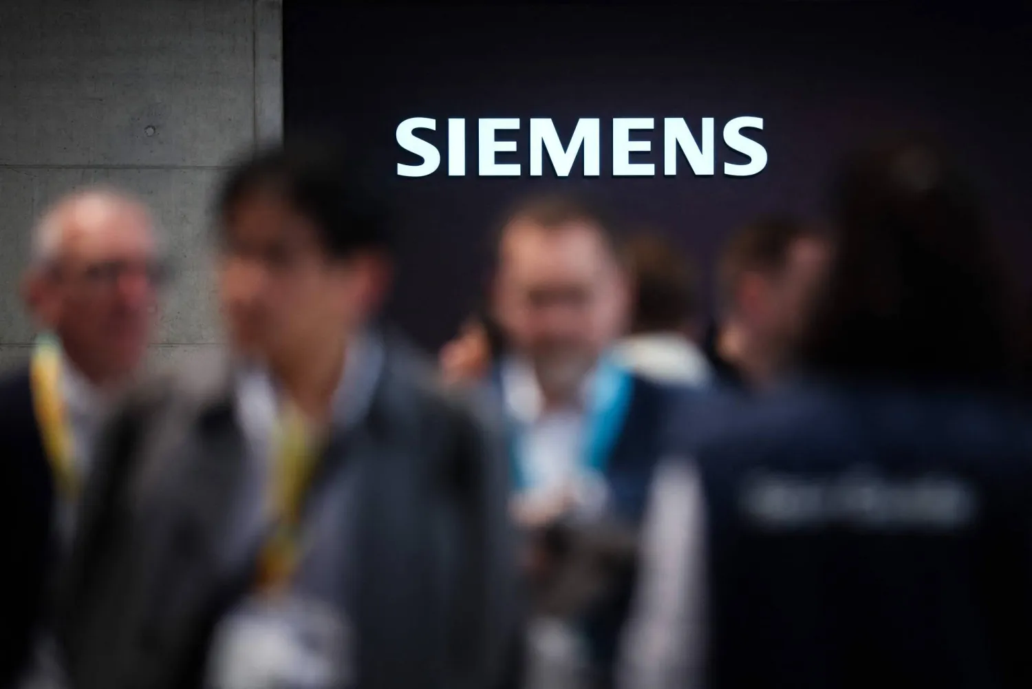 (FILES) Visitors are seen at the booth of German industrial conglomerate Siemens with an illuminated logo during the Hannover industrial trade fair for mechanical and electrical engineering and digital industries, in Hannover, northern Germany on April 20, 2026. (Photo by RONNY HARTMANN / AFP)