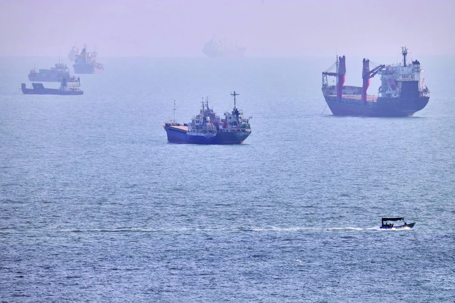 Bender Abbas açıklarında, Hürmüz Boğazı'nda demirlemiş kargo gemileri ve ticari tankerlerin yakınında küçük bir tekne seyrediyor (AP)