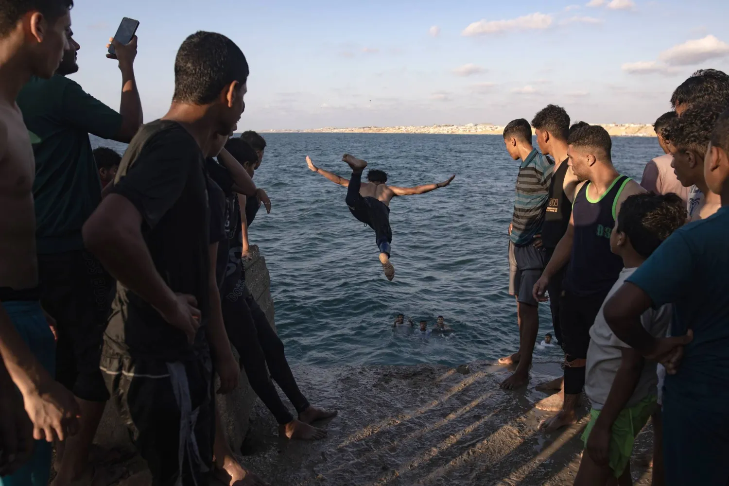 فلسطينيون يراقبون شاباً يقفز إلى البحر في خان يونس جنوب قطاع غزة يوم الجمعة (إ.ب.أ)