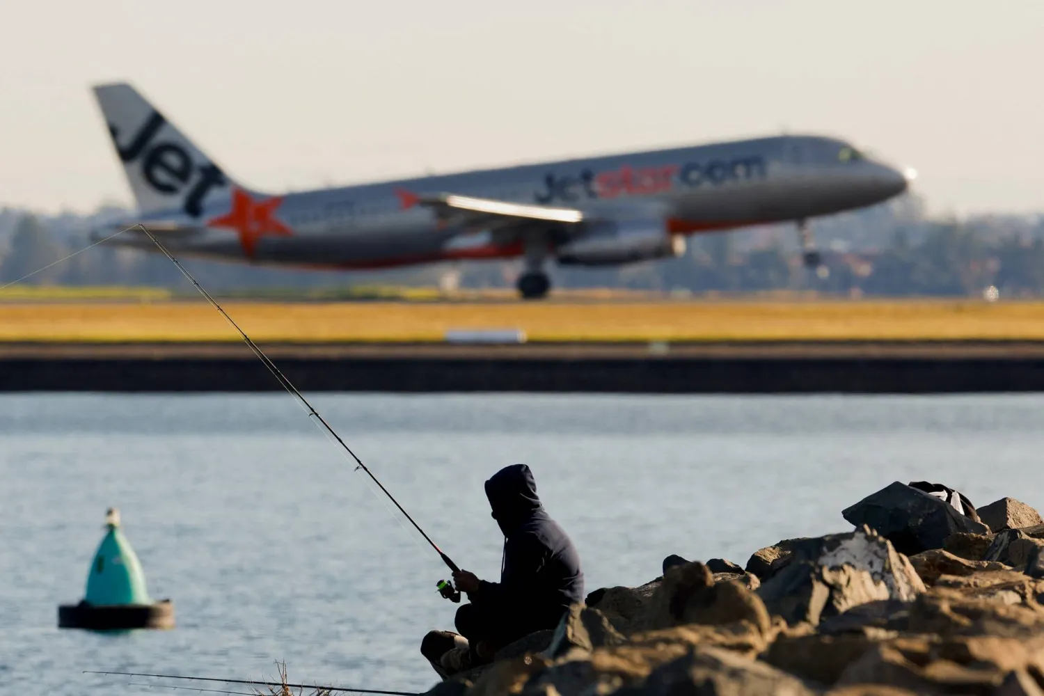 A person uses a fishing pole as a Jetstar plane takes off in the background from Sydney International Airport, in Sydney, Australia, August 6, 2026. REUTERS/Izhar Khan