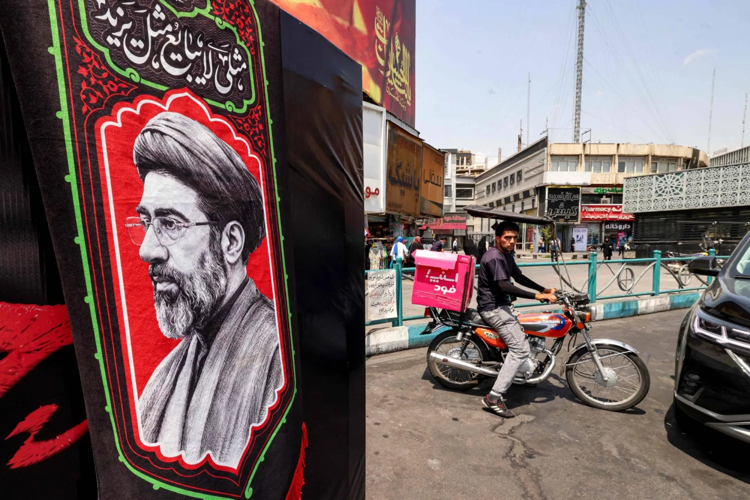 A delivery person rides a motorcycle near an image of Iran's Supreme Leader Mojtaba Khamenei at Valiasr Square in central Tehran on August 8, 2026. (AFP)