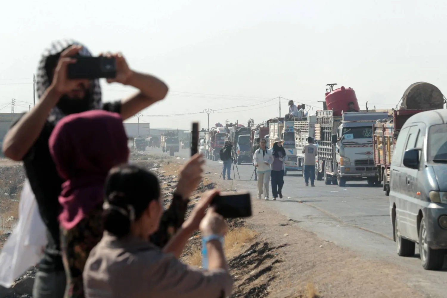 Onlookers take pictures of Syrian Kurds, who were living in displacement camps in the city of Hasakeh, heading back to the northeastern border town of Ras al-Ain on August 10, 2026. (AFP)