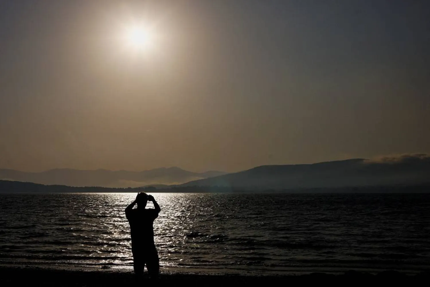 A tourist photographs the sun with his mobile phone at Arija beach, Spain, August 11, 2026. (Reuters)