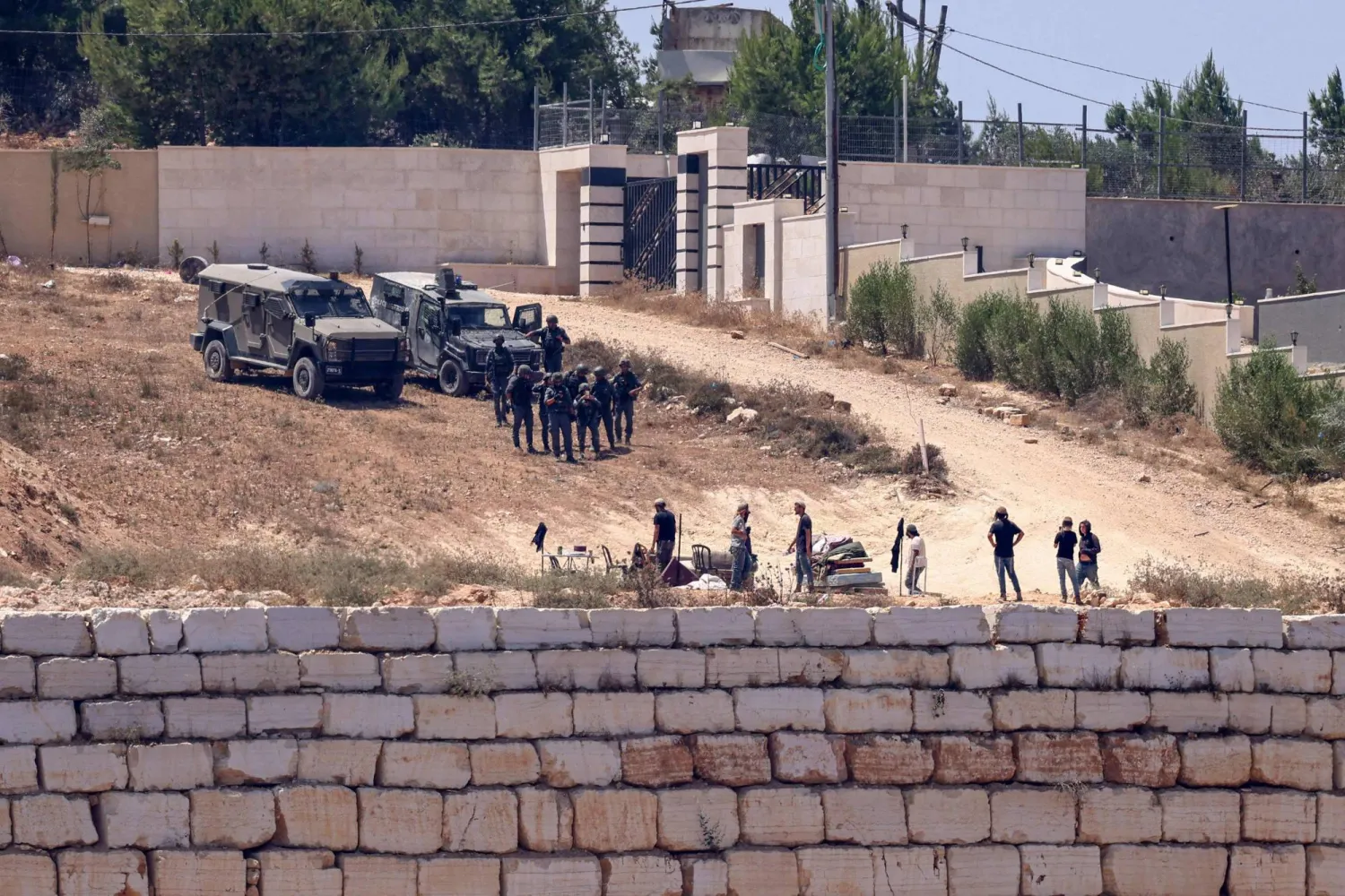 جنود إسرائيليون ومستوطنون يقفون أمام منازل فلسطينية في بلدة قصرة جنوب نابلس بالضفة الغربية يوم الأربعاء (أ.ف.ب)
