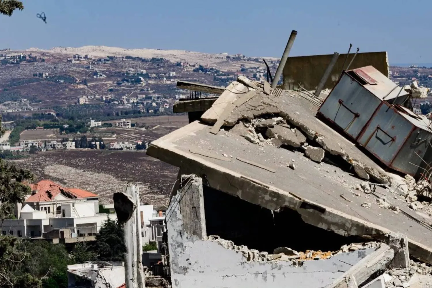 Rubble of homes in the town of Mayfadoun, with traces of a large explosion that struck in southern Lebanon seen in the background (Asharq Al-Awsat)