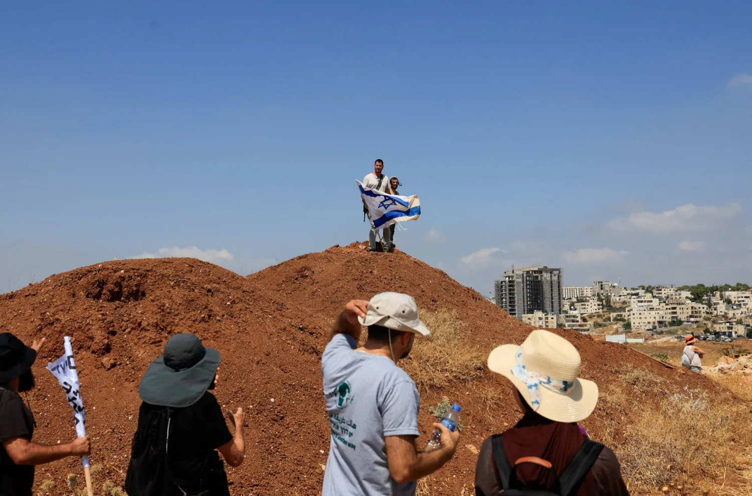 Armed Israeli settlers holding an Israeli flag look on as Palestinian and Israeli activists accompany Palestinian landowners in their property, which is threatened with confiscation by Israeli settlers, in Beit Sahour in the Israeli-occupied West Bank August 14, 2026. REUTERS/Mussa Qawasma
