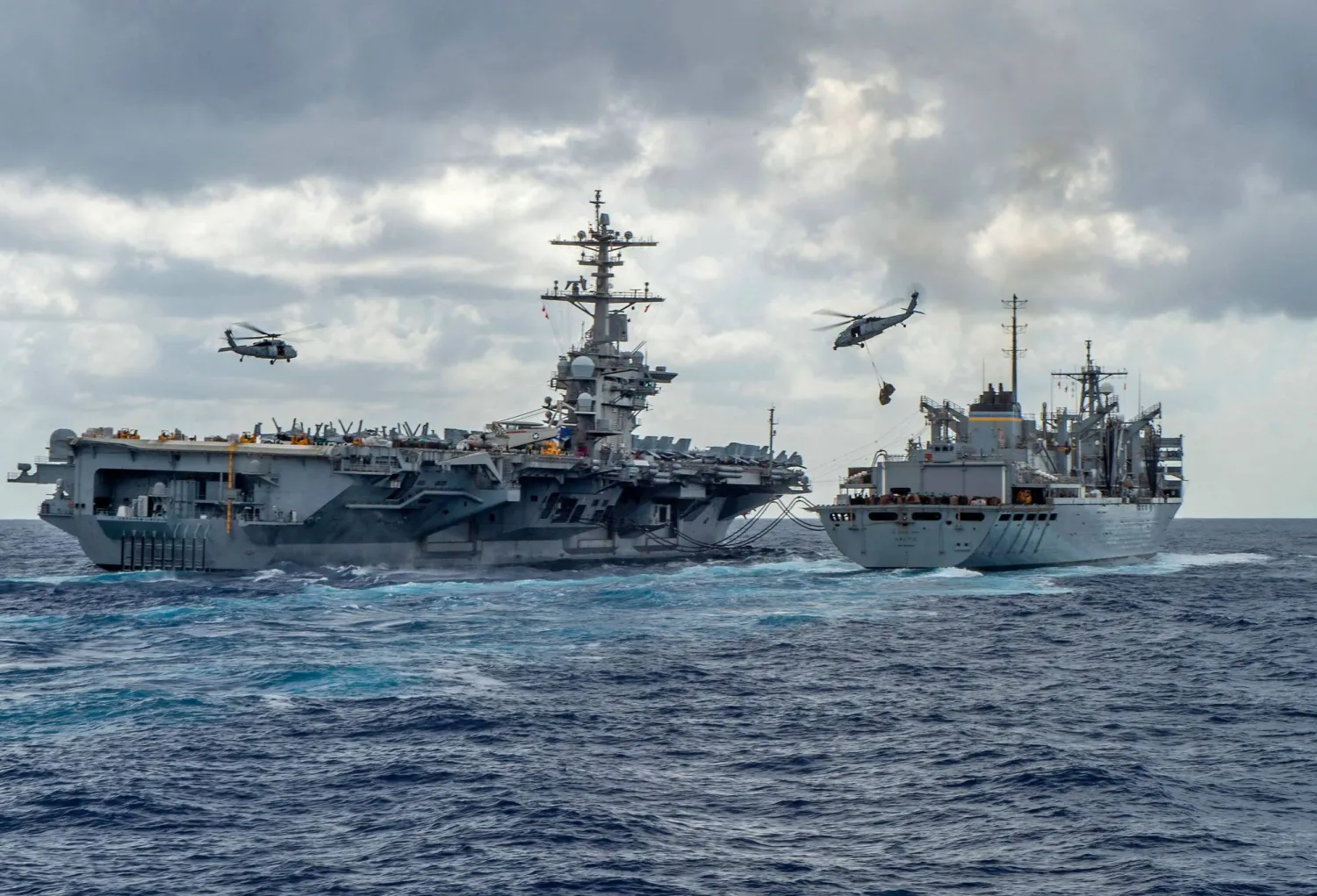 This handout picture released by the US Navy on May 8, 2019 shows the Nimitz-class aircraft carrier USS Abraham Lincoln (CVN 72) while conducting a replenishment-at-sea with the fast combat support ship USNS Arctic (T-AOE 9), while MH-60S Sea Hawk helicopters assigned to the "Nightdippers" of Helicopter Maritime Strike Squadron (HSM) 5, transfer stores between the ships. (Jason WAITE / Navy Office of Information / AFP) 