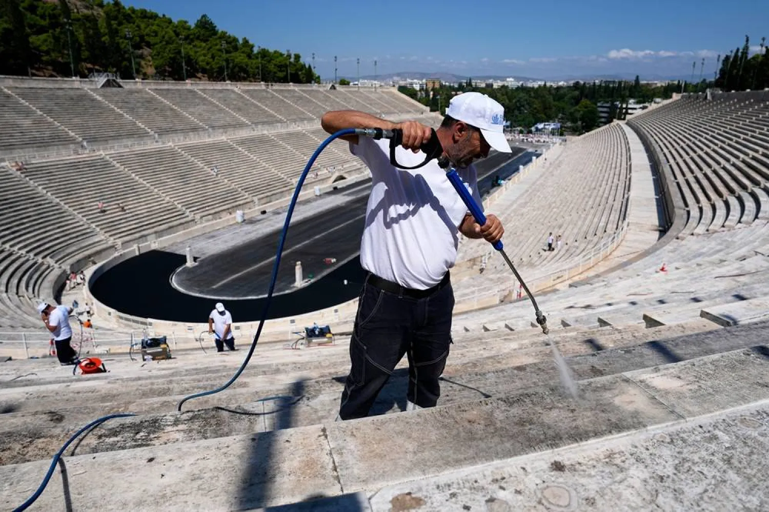 A worker cleans the marble surfaces of the Panathenaic Stadium, also known as "Kallimarmaro," or beautiful marble, which hosted the first modern Olympic Games in 1896, using a high-pressure water hose during renovation work in Athens, Greece, Thursday, Aug. 13, 2026. (AP Photo/Thanassis Stavrakis) 