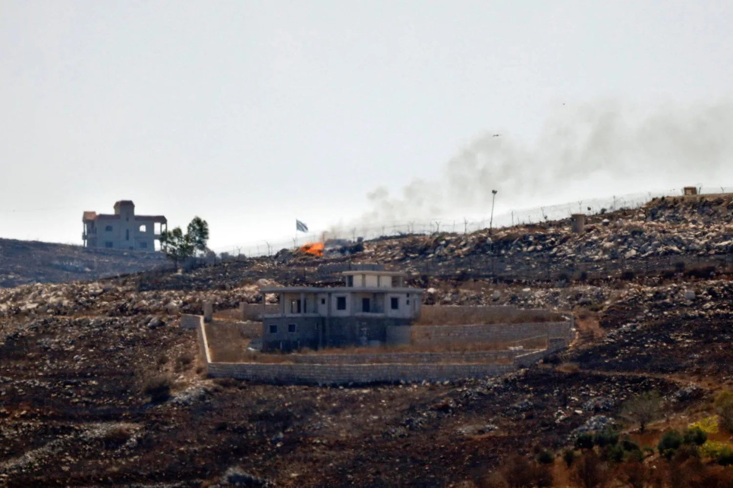 A photograph taken from the southern Lebanese village of Chaqra shows an Israeli flag fluttering over the burnt fields of the border village of Mais al-Jabal, burnt during Israeli military operations on August 11, 2026. (AFP)