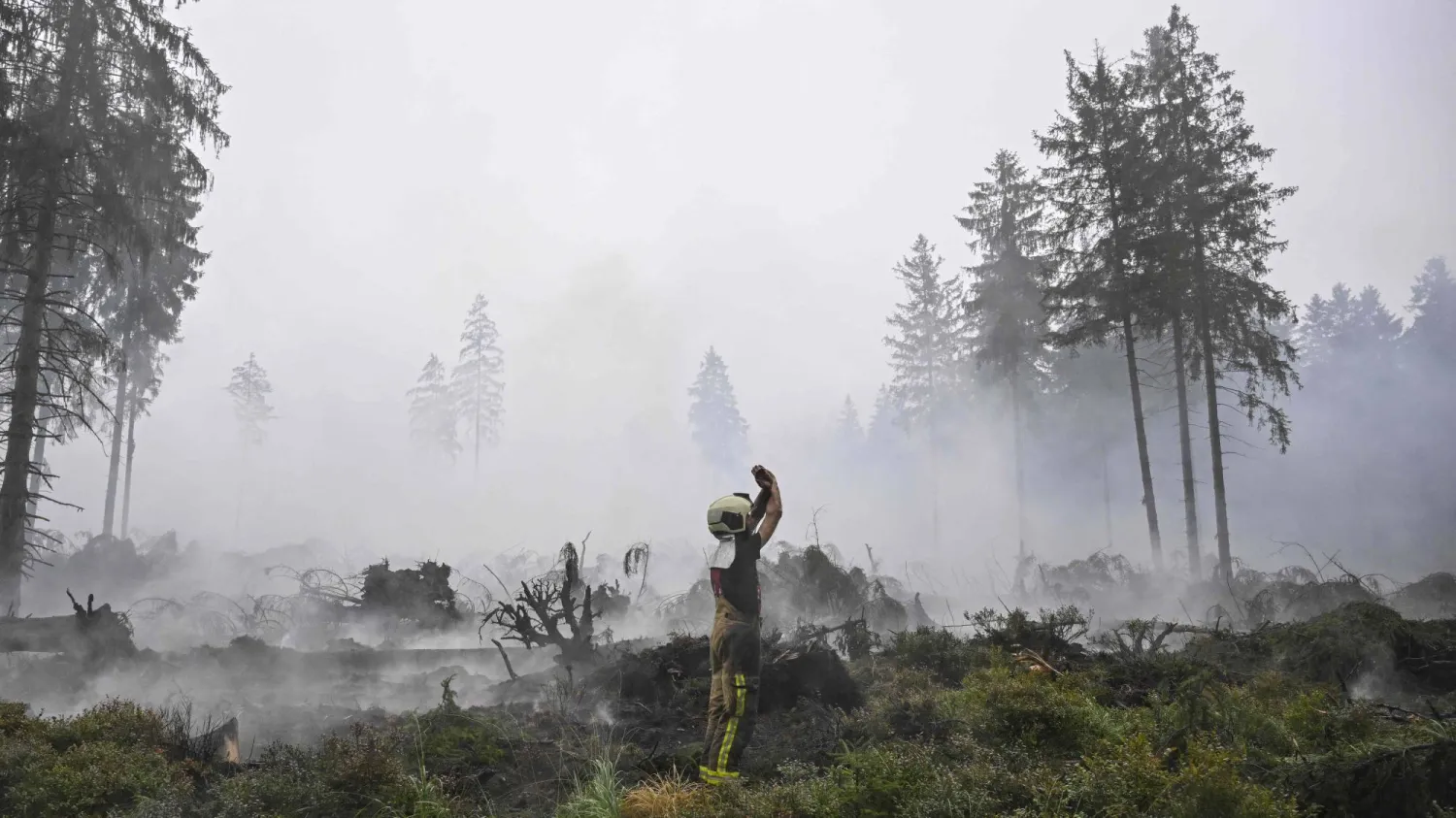 A firefighter gestures to another as smoke emanates from burnt vegetation during operations against a wildfire at the Hautes Fagnes (High Fens) nature reserve near Baelen, on August 18, 2026. (AFP)