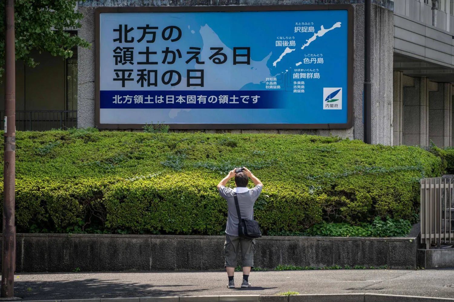 A man takes photographs of a Japanese government sign reading "Day of the Return of the Northern Territories, Day of Peace. The Northern Territories are an inherent part of Japan's territory." (Photo by Yuichi YAMAZAKI / AFP)