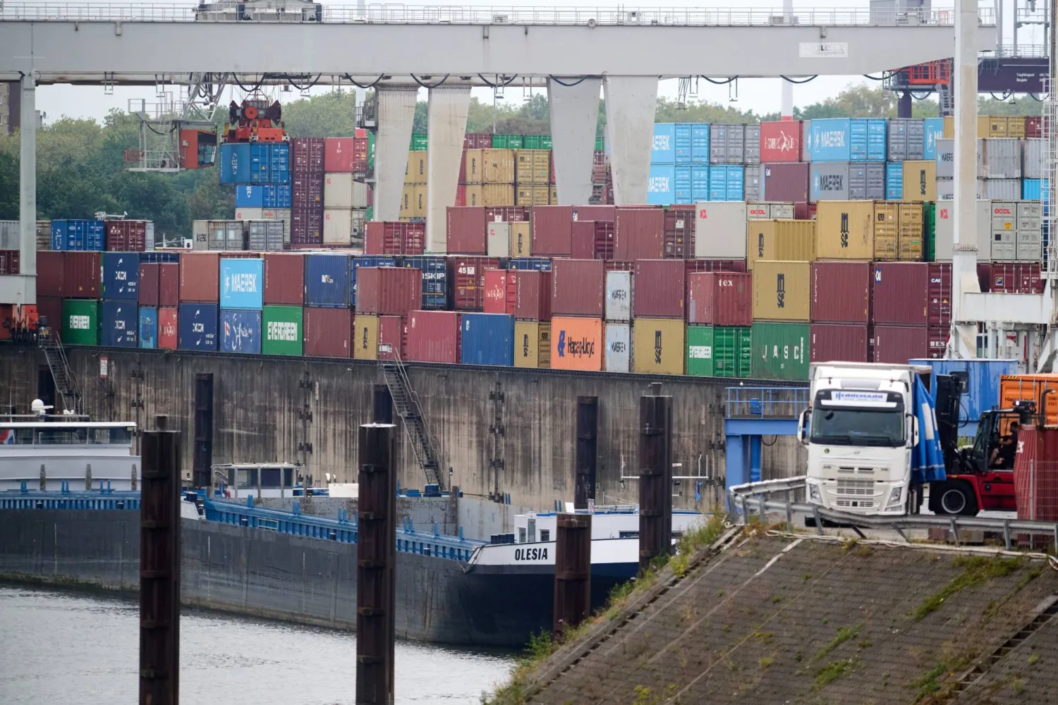 PRODUCTION - 19 August 2026, North Rhine-Westphalia, Duisburg: A truck is being loaded with a forklift at the Duisport Port in Duisburg while a ship is at anchor. Photo: Bernd Thissen/dpa