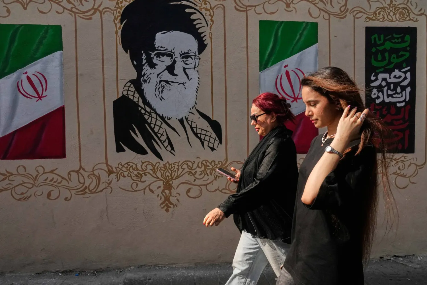 إيرانيتان تمران قرب صورة للمرشد الإيراني السابق علي خامنئي، الذي قُتل في الضربات الأميركية - الإسرائيلية في 28 فبراير، وأعلام إيرانية وسط طهران 20 أغسطس 2026 (أ.ب)