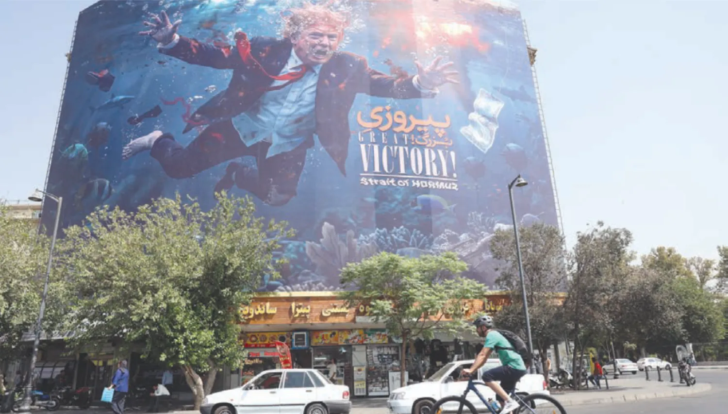 Motorcyclists pass a billboard depicting US President Donald Trump underwater amid explosions, with the words “Great Victory! Strait of Hormuz,” in Tehran, Iran (EPA)