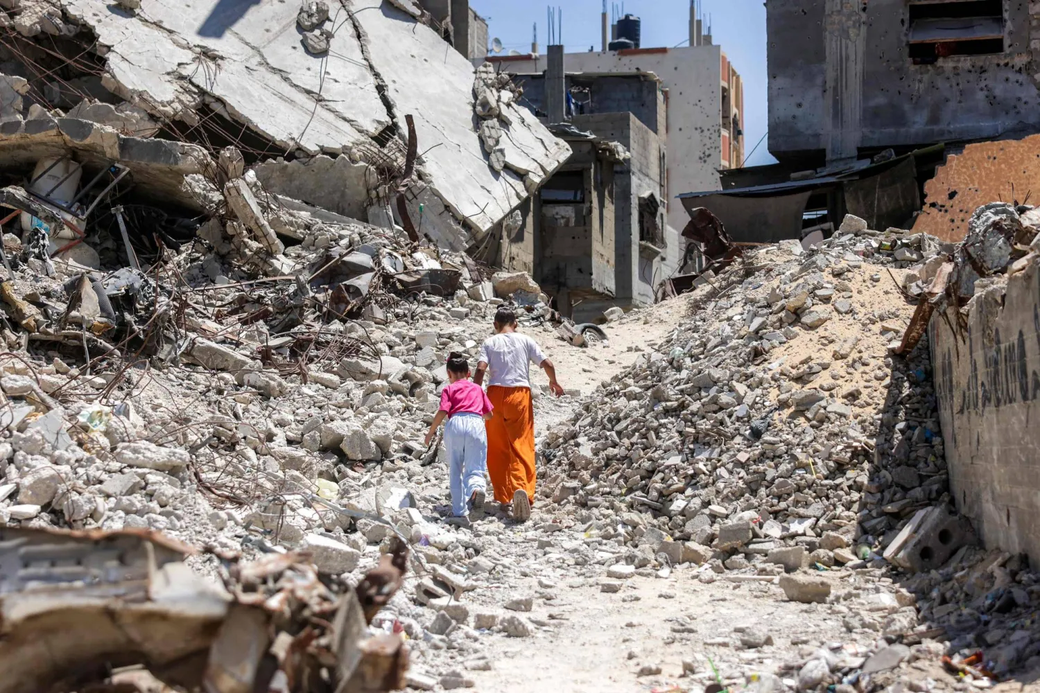 TOPSHOT - Two girls walk past the rubble of collapsed buildings in Khan Yunis in the southern Gaza Strip on August 25, 2026. (Photo by Bashar Taleb / AFP)