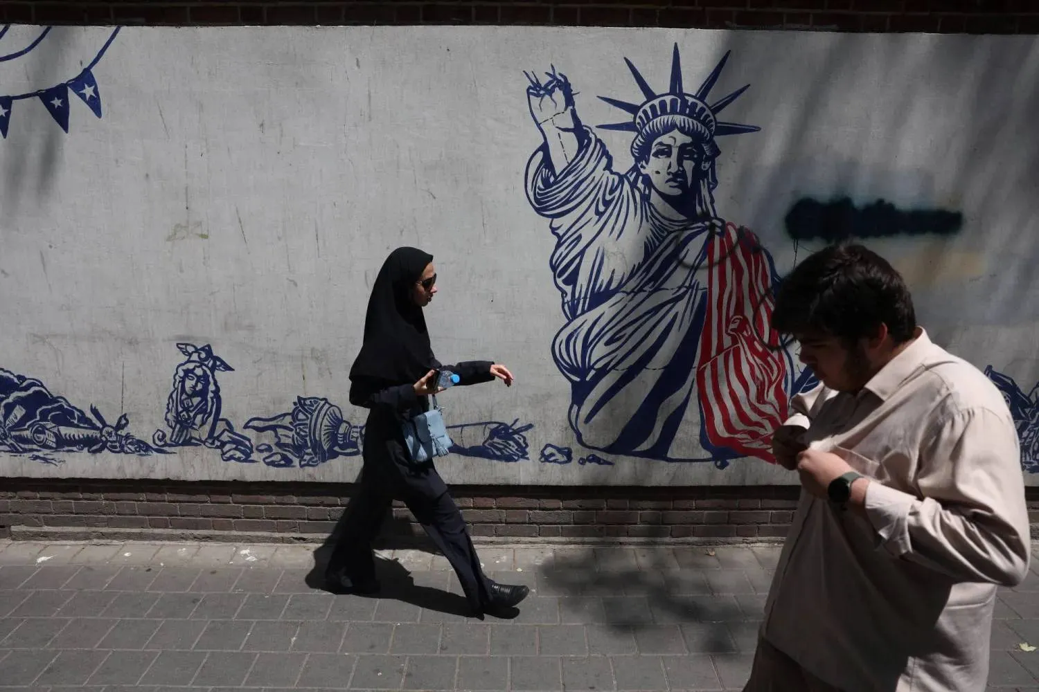  İranlılar Tahran'da Amerikan karşıtı bir duvar görselinin önünden geçiyor - 15 Temmuz 2026 (Reuters)