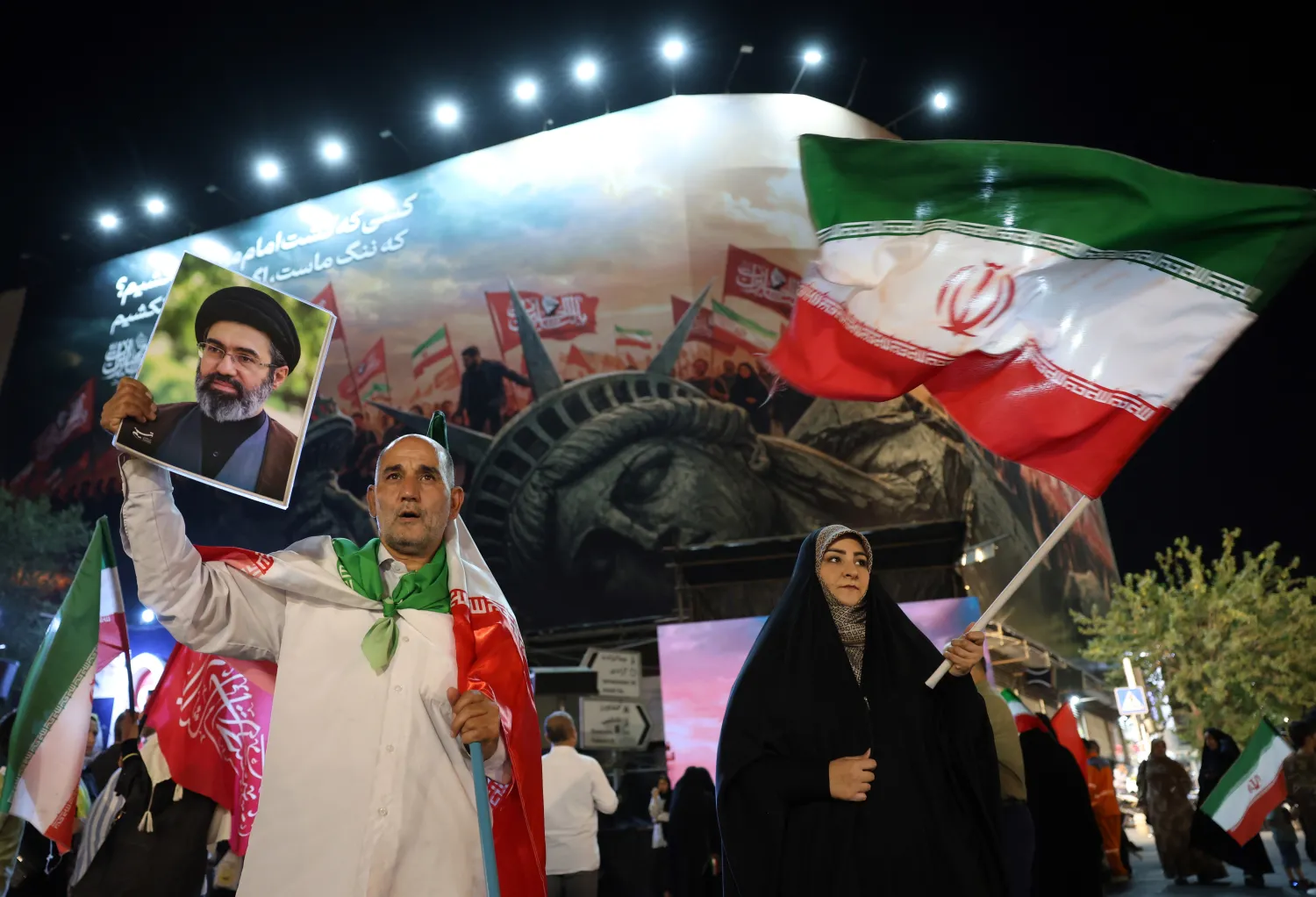 An Iranian man (L) holds a portrait of Supreme Leader Mojtaba Khamenei during a night demonstration against the United States in Tehran, Iran, 26 August 2026, following Washington's announcement of new sanctions. (EPA) 
