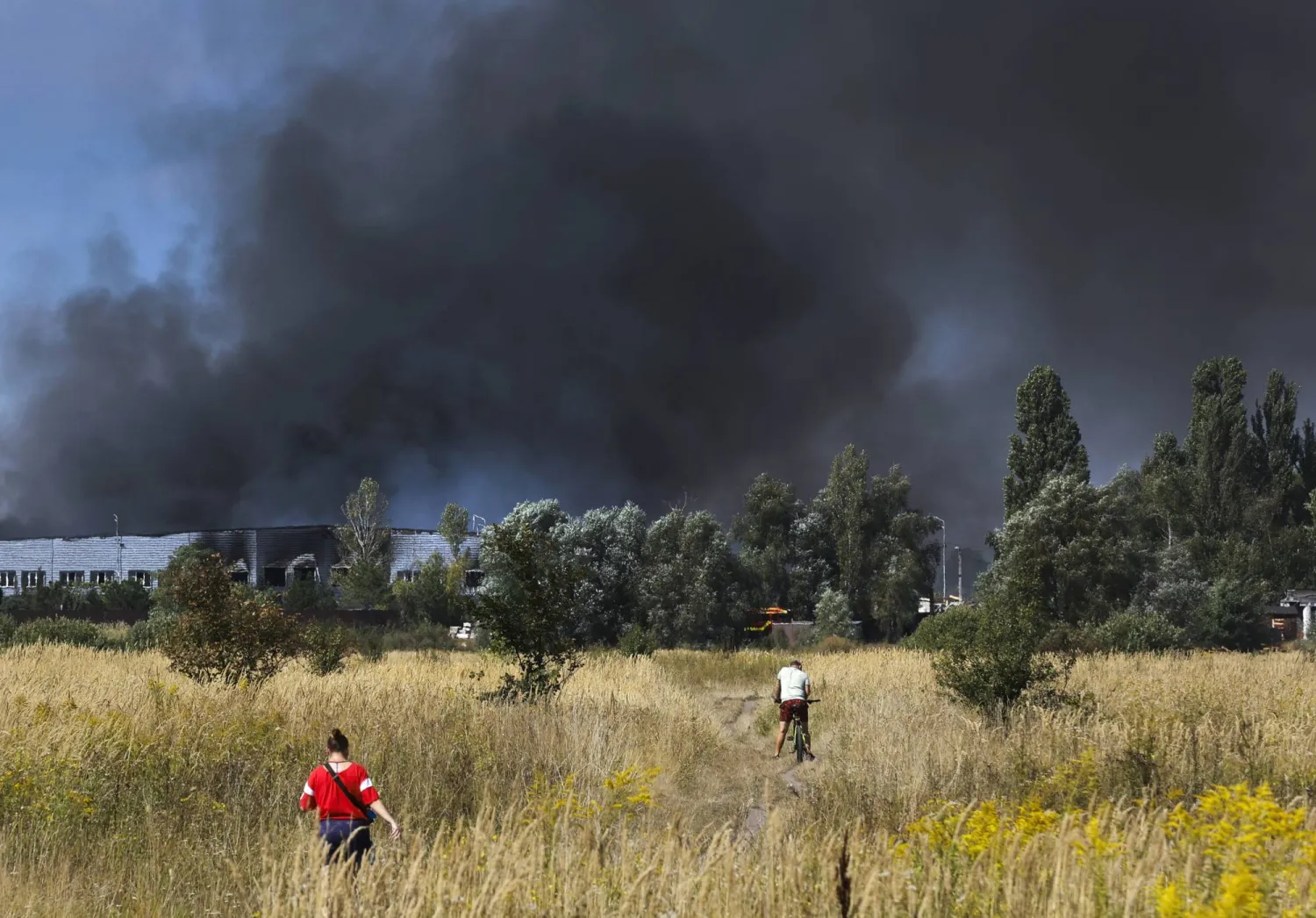 People walk on a field as smoke rises at the site of a Russian strike near Kyiv, Ukraine, 31 August 2026, amid the Russian invasion. (EPA)