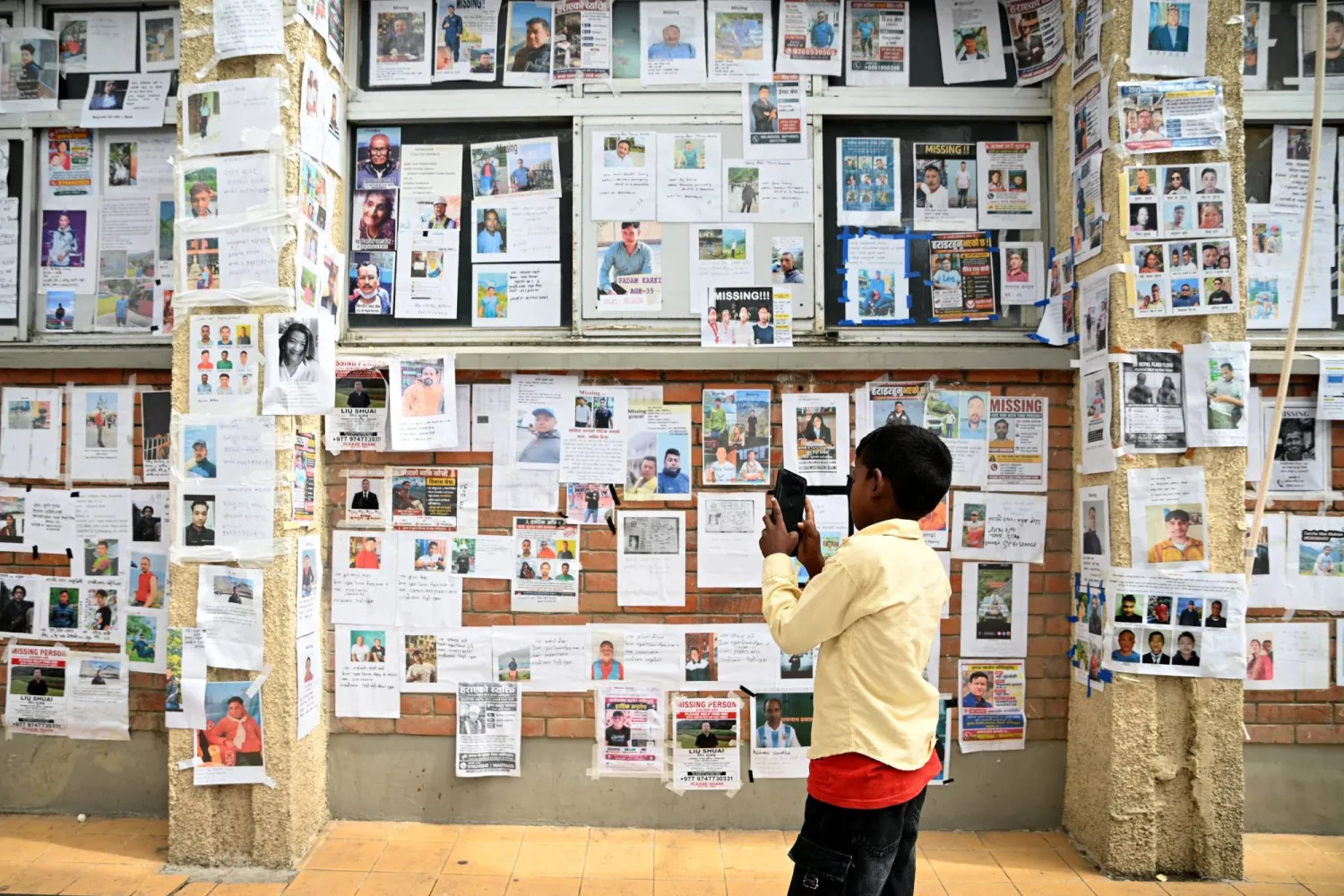A boy uses a mobile phone to take photos of missing and deceased people pasted on wall outside Tribhuvan University Teaching Hospital, following flash floods and a mudslide, in Kathmandu, Nepal, September 1, 2026. (Reuters)