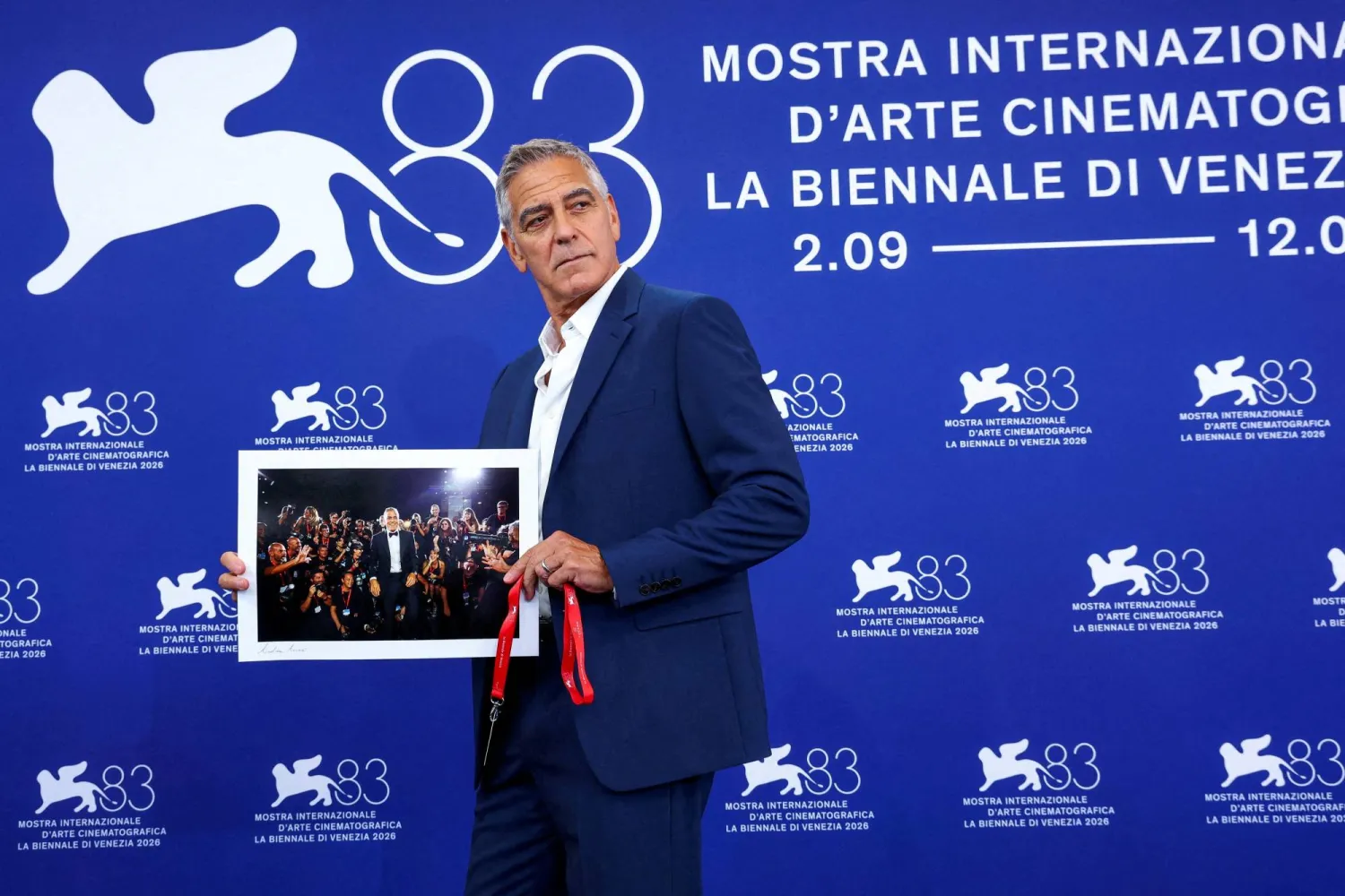 جورج كلوني يرفع صورة له من مهرجان البندقية السينمائي السابق خلال جلسة تصوير في الدورة الثالثة والثمانين لمهرجان البندقية السينمائي في البندقية - إيطاليا 2 سبتمبر 2026 (رويترز)