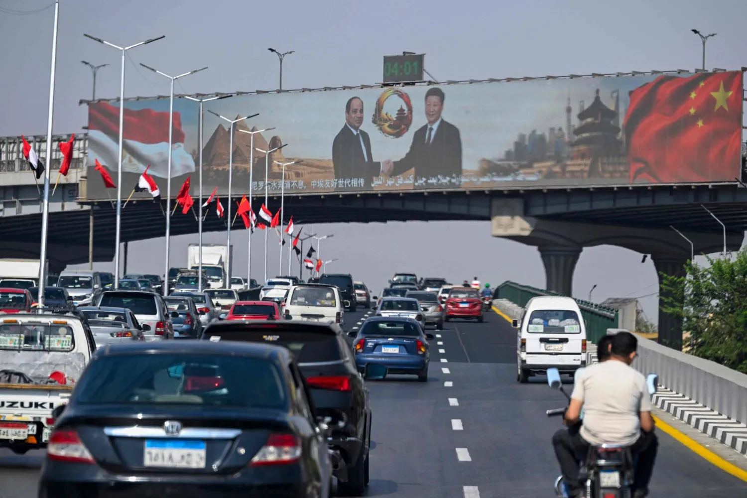 تمر سيارات أسفل شاشة عرض كبيرة تعرض صور الرئيس المصري عبد الفتاح السيسي ونظيره الصيني شي جينبينغ في القاهرة (أ.ف.ب)