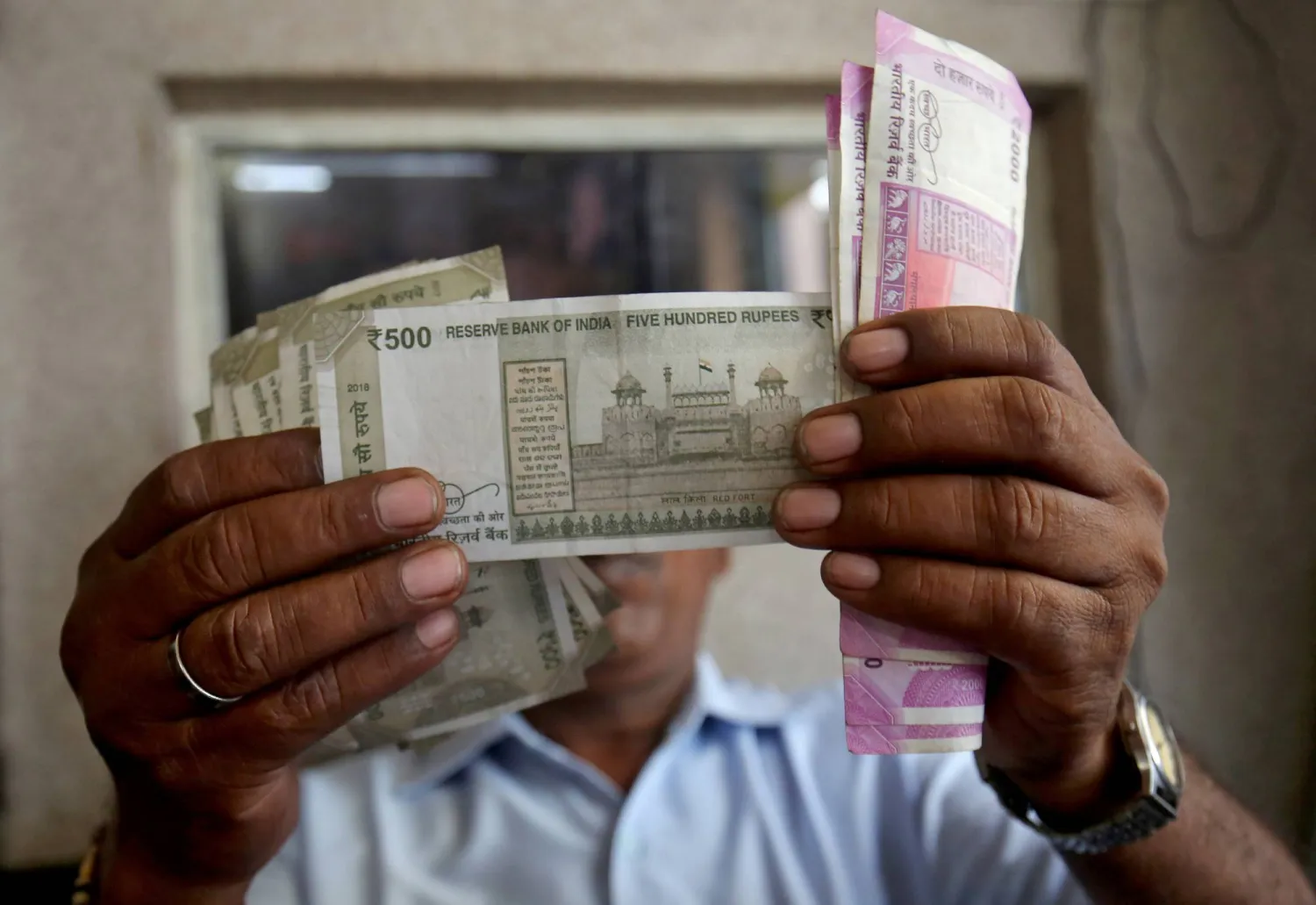 يتحقق أمين صندوق من أوراق نقدية بالروبية الهندية داخل غرفة بمحطة وقود في أحمد آباد (رويترز)