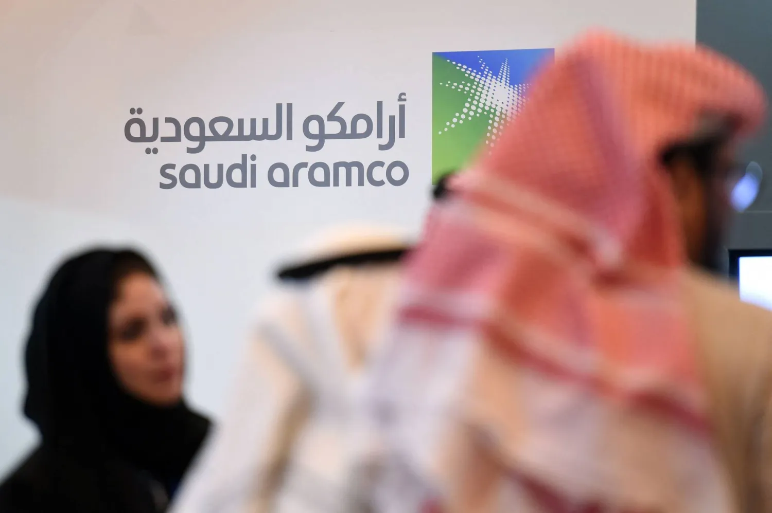 أشخاص يقفون أمام شعار شركة «أرامكو» خلال المنتدى العالمي العاشر للتنافسية (أرشيفية - أ.ف.ب)