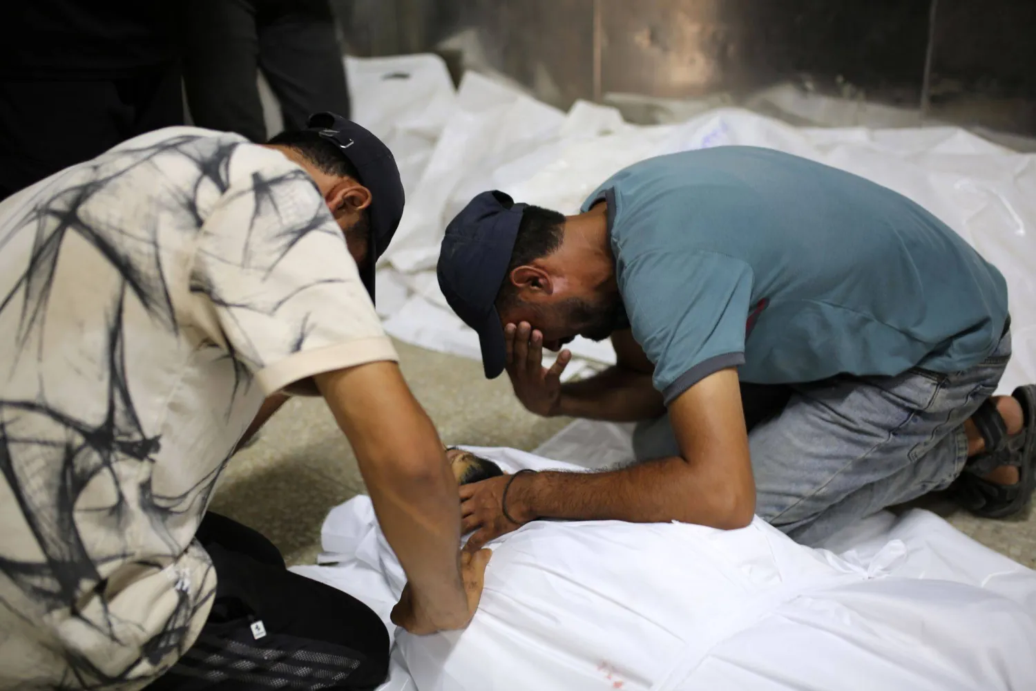 فلسطينيان يبكيان فوق جثمان آخر في مستشفى الشفاء بمدينة غزة يوم الخميس بعد مقتله في غارة إسرائيلية (د.ب.أ)