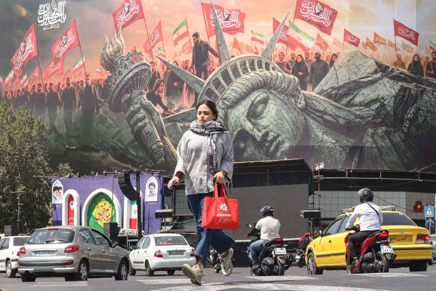A woman crosses as motorists drive past an anti-US billboard at Enghelab Square in Tehran on September 2, 2026. (AFP)