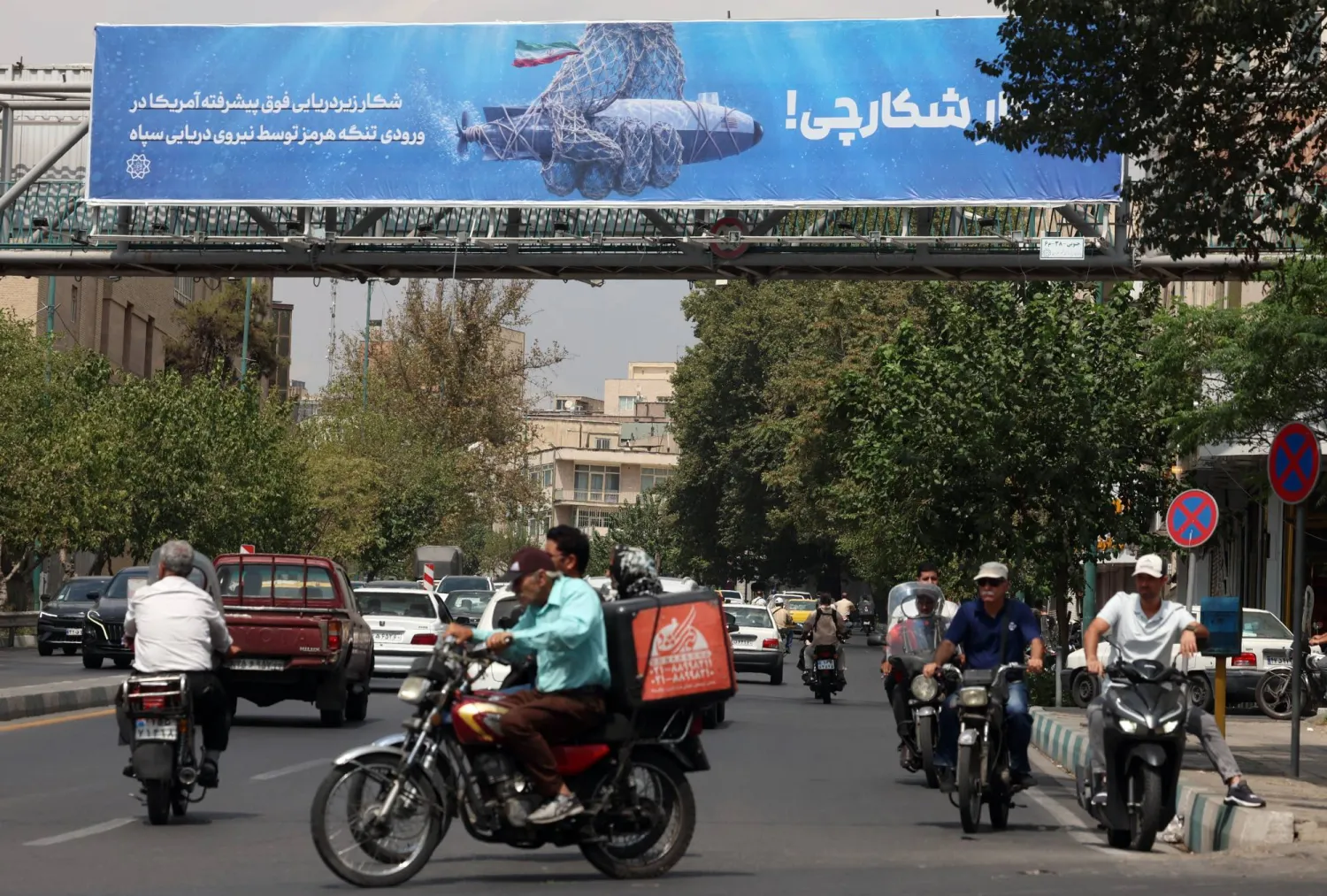 إيرانيون يمرون أمام لوحة دعائية في طهران تُظهر مسيّرة أميركية تحت الماء قال «الحرس الثوري» إنه استولى عليها وتحمل عبارة «صيد الصياد» 9 سبتمبر 2026 (إ.ب.أ)