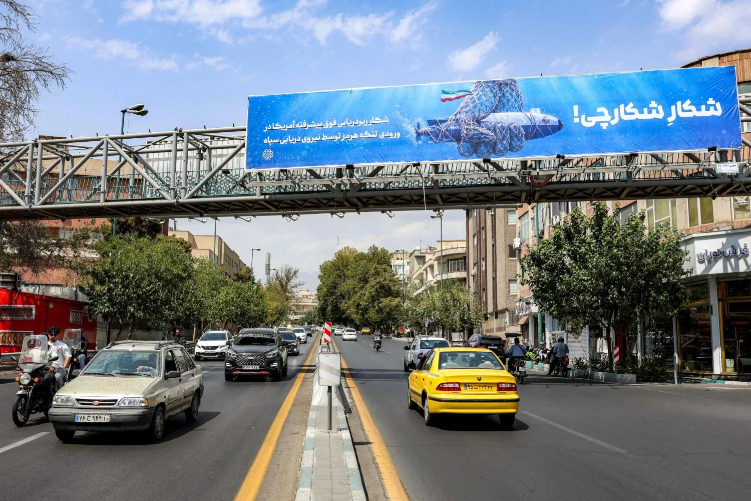 سيارات تتحرك على طول شارع بالقرب من جسر للمشاة يحمل لوحة إعلانية مناهضة لأميركا في طهران (أ.ف.ب)
