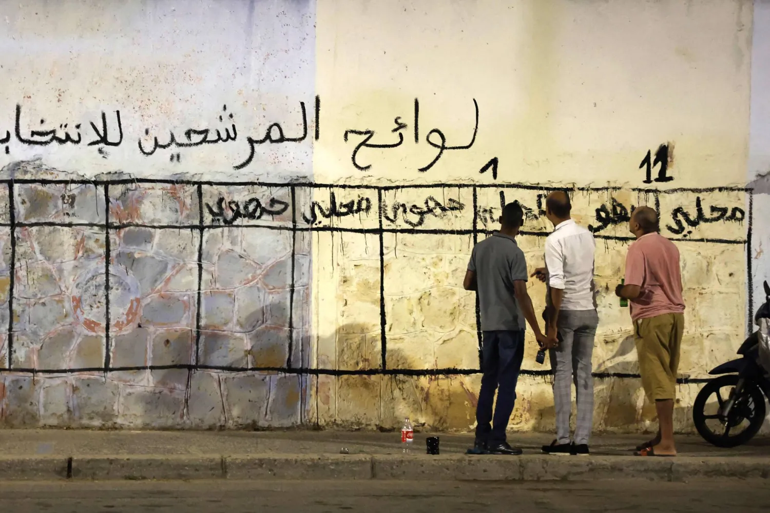 شُبان مغاربة أمام حائط خُصّص لحملة الانتخابات التشريعية (أ.ف.ب)