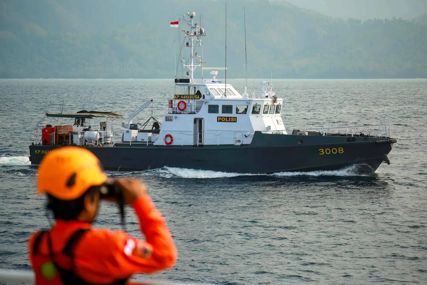 A police boat is seen as a team member uses binoculars during search operations for a speedboat carrying eight people including five journalists, which went missing September 7 in waters of the Sunda Strait, on September 12, 2026.  (Photo by PERDIANSYAH / AFP)