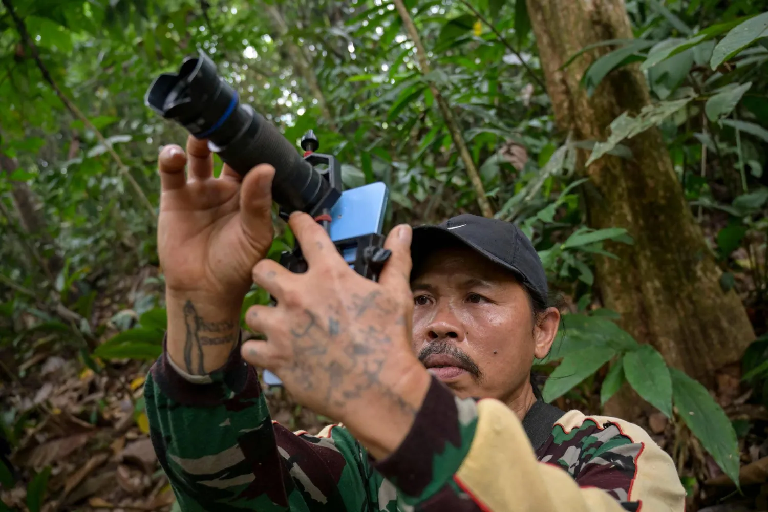 This picture taken on September 2, 2026 shows wildlife observer and former poacher Octavius using a mobile phone equipped with a telephoto lens to take pictures of wildlife in a forest near Labian village in Kapuas Hulu, West Kalimantan. (Photo by BAY ISMOYO / AFP)