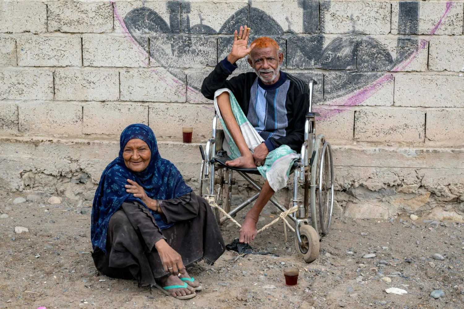  مسن يمني يجلس على كرسي متحرك بجوار امرأة بمركز إيواء مؤقت للنازحين في عدن (أ.ف.ب)