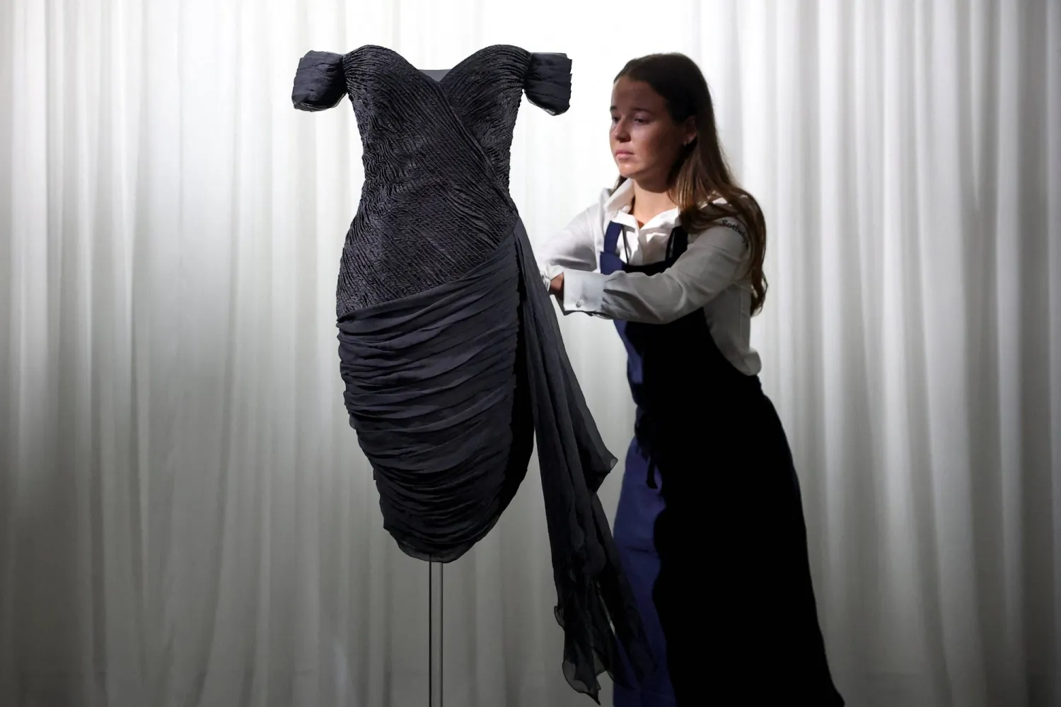 A Sotheby’s employee adjusts Princess Diana's "Revenge Dress" by Greek designer Christina Stambolian in London, Britain, September 18, 2026. REUTERS/Toby Melville
