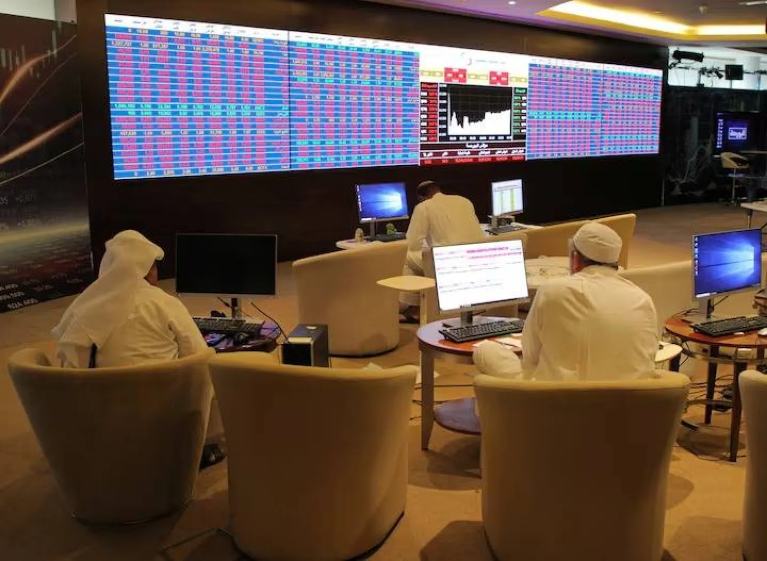 مستثمرون في قطر يتابعون أسعار الأسهم على شاشة التداول ببورصة الدوحة (رويترز)