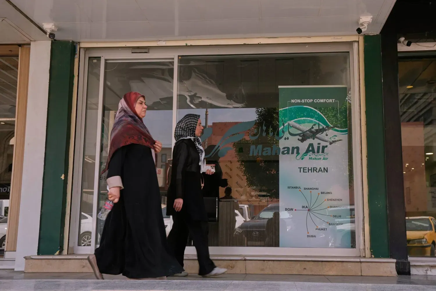İran hava yolu şirketi Mahan Air’in Bağdat’taki ofisinin önünden geçen yayalar (AP)